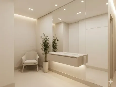 Recepção pequena e bem organizada de uma clínica de estética, com um espelho grande na parede para criar sensação de amplitude e móveis verticais.